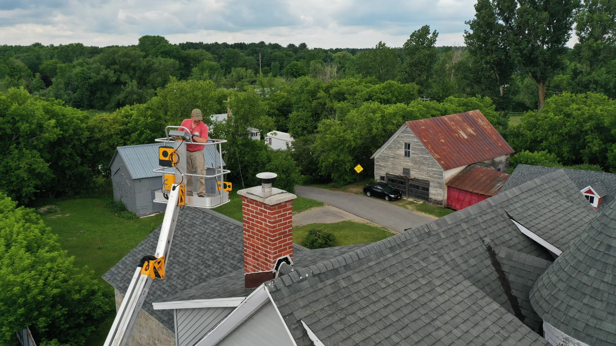 AFE fieldwork photograph showing a technician in an aerial lift beside a chimney and North Country buildings